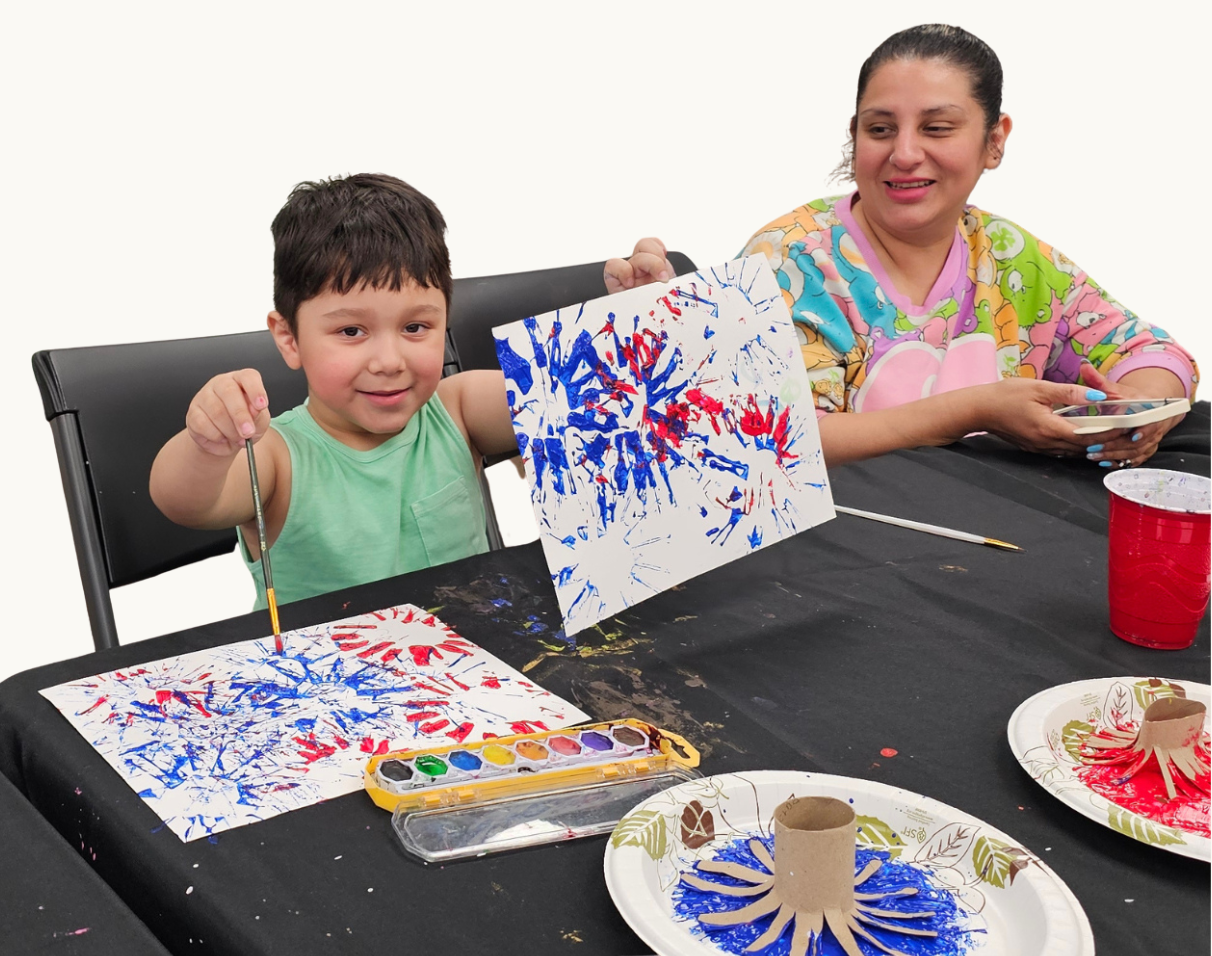 child-art-class.png Child proudly displaying artwork created during a Variety of the Desert art program while a caregiver participates.
